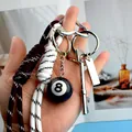 Keyring with black 8-ball billiard charm and woven ropes held in hand for scale - Brown And White Cord With Tag