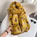 Close-up of ginger knit scarf with cat patterns and short fringe detail on white chair - Yellow