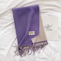 Detalle de bufanda reversible morada y avena con flecos y etiqueta de la marca - Morado