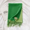 Detail of green cashmere-feel scarf showing soft texture, fringe edges and woven brand label - Grass Green