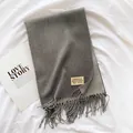 Close-up of thick dark grey scarf texture with long tassels and woven brand label - Gray