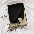Close-up of dual-sided knit scarf in black and beige with fringe and brand label detail - Black