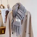 Close-up of grey knit scarf with fringe and logo tag styled on a wool coat - Fish Tail Grey
