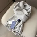 Primer plano de bufanda de lana gris claro con flecos suaves y etiquetas de producto - Gris claro