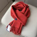 Detalle de bufanda gruesa de lana roja con flecos suaves y etiqueta tejida premium - Rojo Ladrillo