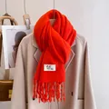 Close-up of bright orange knitted scarf with fringes and logo patch on wool coat - Pumpkin Orange