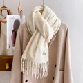 Close-up of cream knit scarf featuring soft texture, long tassels, and a minimalist fabric label - White