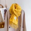 Close-up of ginger yellow knit scarf with fringe tassels and a minimalist brand tag - Lemon Yellow