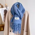 Thick blue knit scarf with decorative tassels and woven label on beige coat - Denim Blue