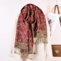 Dettaglio dello scialle rosso con motivo paisley dorato e frange su cappotto beige - Bordeaux