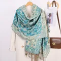 Teal and gold paisley jacquard scarf with elegant tassels styled on a cream coat - Light Lake Blue