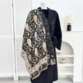 Dikke dames pashmina sjaal met paisley patroon en franjes gedrapeerd over een zwarte jas - Zwart