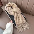 Close-up of the plush cashmere-like plaid scarf with fine fringes on a leather couch - Beige