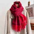 Détail d'une écharpe en maille rouge avec motifs de lettres et franges sur un manteau beige - Type standard / Rouge