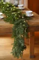 Detail of lush green PE Christmas garland with warm LED lights on a rustic wooden table - D Style (With Lights)