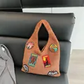 Brown knit tote bag with vintage American cryptid embroidered patches on a leather sofa - Brown