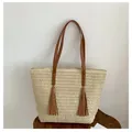 Detail of woven straw tote bag featuring brown leather straps and stylish fringe tassels - Beige