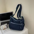 Donkerblauwe denim crossbodytas met meerdere ritsen en klinknagels op een wit bureau - Donkerblauw