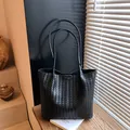 Black woven leather tote bag with dual shoulder straps in a minimalist aesthetic - Black