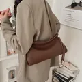 Detalle del bolso de cuero marrón oscuro con aros dorados sobre un blazer beige - café