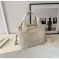 Cream canvas tote with wide handles and adjustable strap shown in a minimal indoor setting - Off White