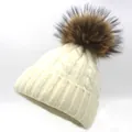 Close-up of beige knit beanie featuring thick cable patterns and large raccoon fur pom-pom - Off White