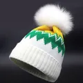 Detaillierte Strickstruktur und flauschiger Pelzbommel an bunter Winterstrickmütze - Gelbgrün