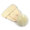 Nahaufnahme der beigen Strickmütze mit Rautenmuster und flauschigem Bommel-Detail - M (56-58cm) / Gebrochenes Weiß
