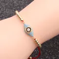 Nahaufnahme des goldenen Evil Eye Armbands mit blauer Einlage und roter Schnur am Handgelenk - Rote Schnur Perlen Böser Blick Stil 5
