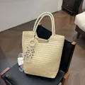 Beigefarbene handgewebte Strohtasche mit Quastenanhänger und Evil-Eye-Perlen auf einem Stuhl - Beige