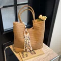 Stroh-Shopper mit Teufelsauge-Quastenanhänger und weißen Tulpen auf Marmorhintergrund - Khaki