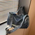 Grote denim schoudertas in acid wash blauw met witte letteropdruk en ritssluiting - Lichtblauw