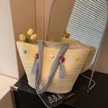 Cremefarbene Strohtasche mit bunten Pompons und blau gestreiftem Griff für den Strand - Beige