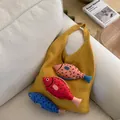 Bolso tote de punto amarillo con dijes de peces coloridos sobre un sofá blanco - Amarillo