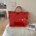 Glossy red hollow-out waterproof tote bag with white text on a white sofa - Red