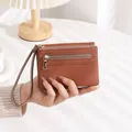 Detailed view of a brown pebbled leather wallet with dual gold zippers and wrist strap - Brown