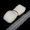 Rotolo di pizzo bianco raffinato con motivo floreale su una superficie nera riflettente - Stile Stretto / Beige
