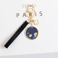 Detailed macro view of navy blue PU leather keychain with embroidered daisy and gold hardware - Blue