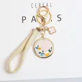 Detail of embroidered daisy round pendant and beige woven strap car keychain with gold hardware - Beige