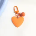 Close-up of a matte orange heart-shaped keychain with matching mini bell and metal carabiner - Orange (a5098-3)