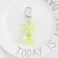 Close-up of a lime green crystal bear keychain with a translucent bow on a white plate - Green