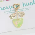 Dettaglio macro del ciondolo a cuore cangiante con moneta Elizabeth II e charm barca a vela - Verde Chiaro Iridescente