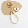 Detail view of pearl bow keychain with gold metal ring and number 5 enamel pendant - White Base Black Bow Style (5182-2)