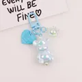 Close-up of blue iridescent bear keychain with heart charm and pearl accessories - Light Blue