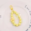 Detail of yellow beaded keychain with 3D cartoon bear and iridescent charms on white plate - Yellow