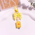 Détail d'un porte-clés nœud jaune avec perles et breloque carte sur plateau blanc - Jaune Vif