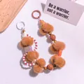 Detail eines Schlüsselanhängers mit braunen Plüschbällen und Perlen auf Texturhintergrund - Khaki