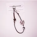 Detail of plaid heart and silver star charms on a brown woven rope phone lanyard strap - Khaki