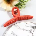 Detail of coral orange matte hair claw clip with cross-teeth design on marble background - Orange