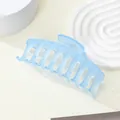 Close-up of matte sky blue hair claw clip on white textured display stand - Blue